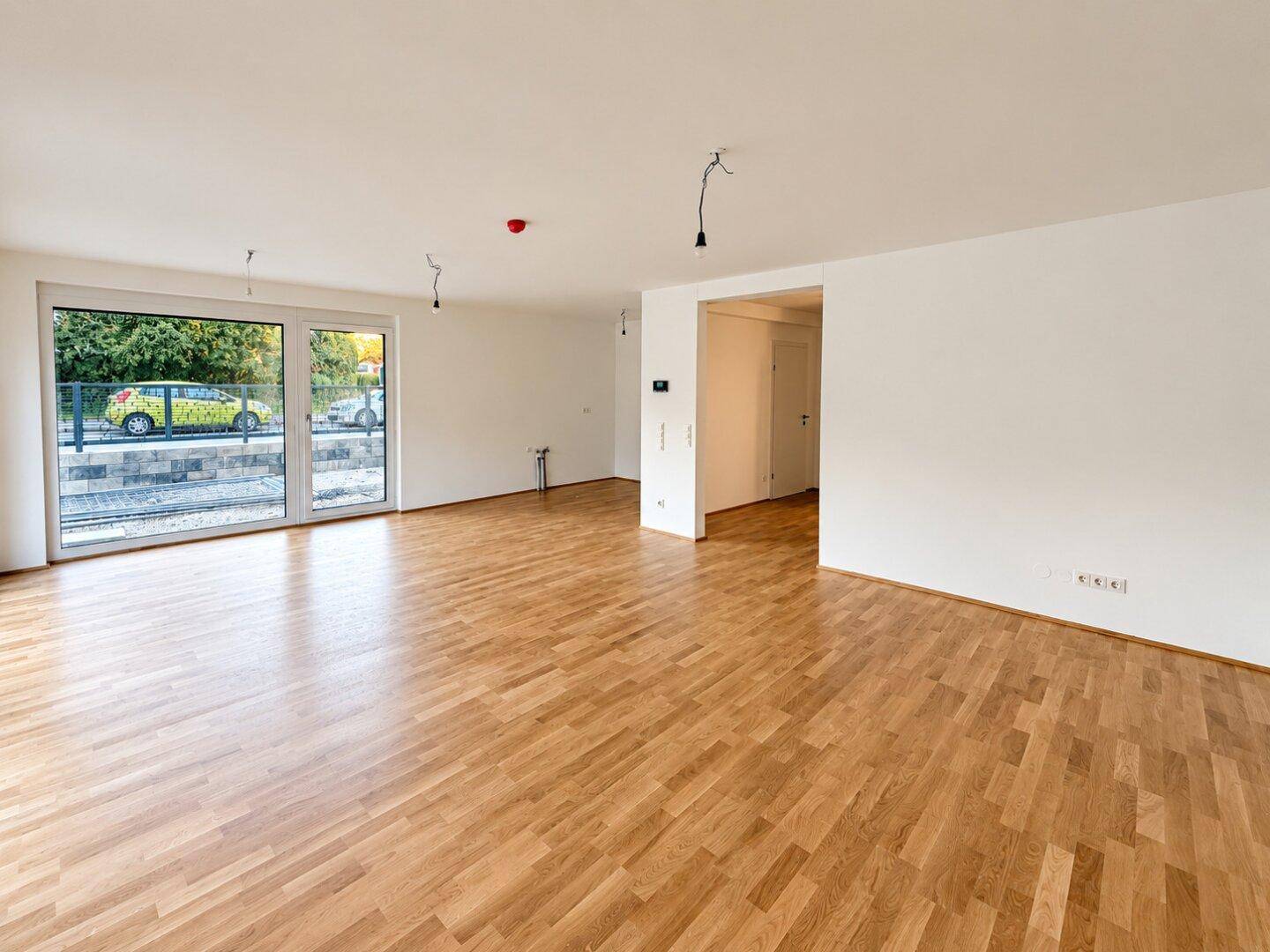Offener Wohnbereich mit Eichenparkettboden und Zugang zu einem Außenbereich durch eine große Glastür.