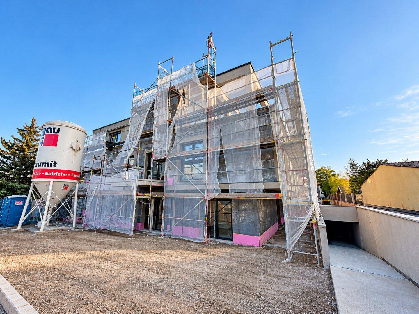 Neubau im Bau mit Gerüst und Baustellenelementen unter blauem Himmel.