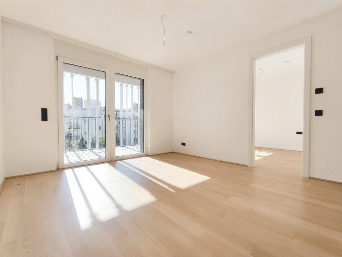 Helles, leeres Zimmer mit Parkettboden und Zugang zu einem Balkon, ideal als Wohnbereich.