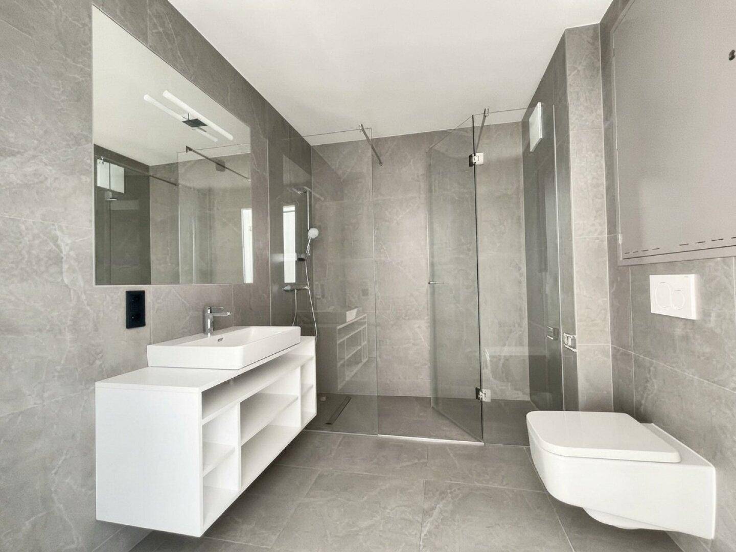 Modernes Badezimmer mit grauen Fliesen, ebenerdiger Dusche und schwebendem Waschtisch.