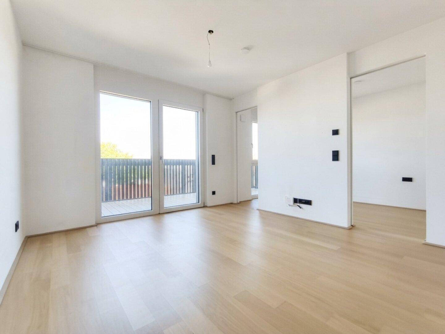 Helles, unmöbliertes Zimmer mit Parkettboden und großen Fenstern zum Balkon.