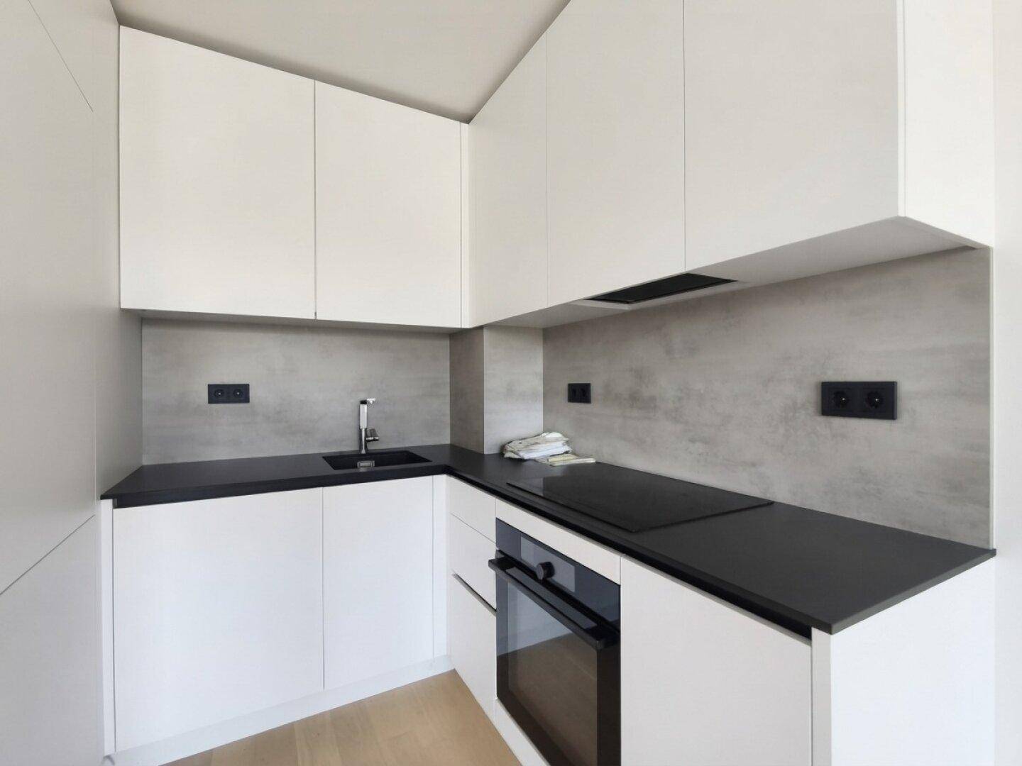 Moderne Einbauküche mit weißen Schränken, dunkler Arbeitsplatte und Induktionskochfeld.
