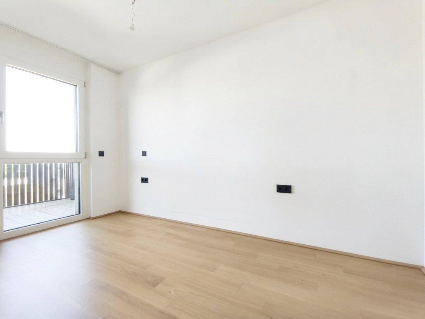 Helles Schlafzimmer mit Parkettboden und großem Fenster, bereit zur individuellen Gestaltung.
