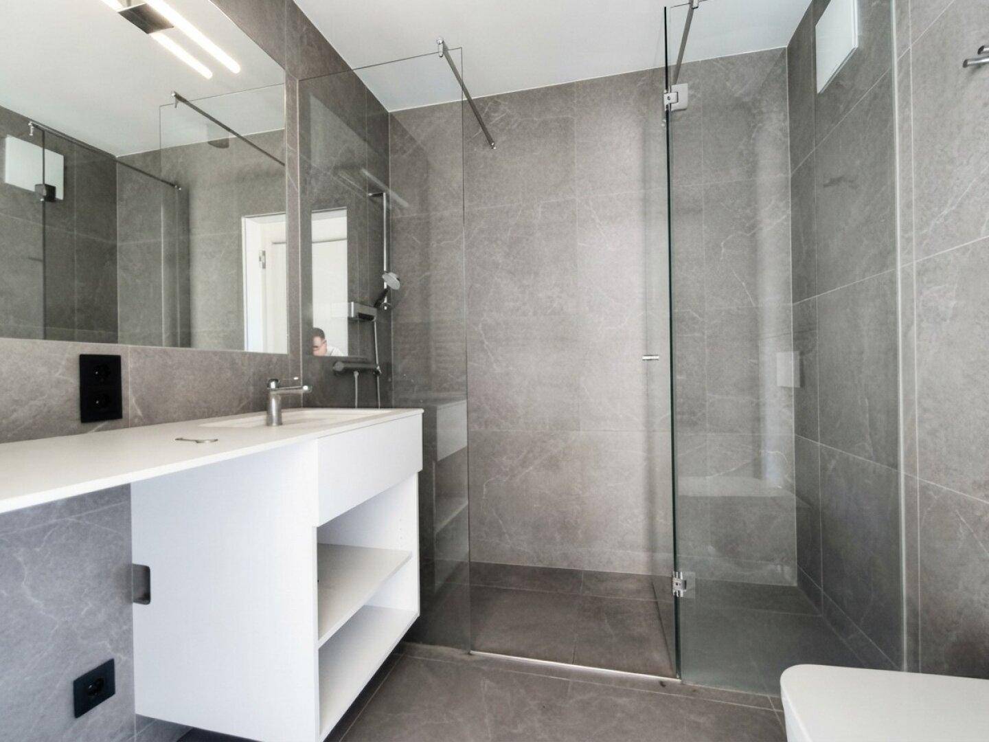 Modernes Badezimmer mit grauen Fliesen, begehbarer Dusche und stilvollem Waschtisch.