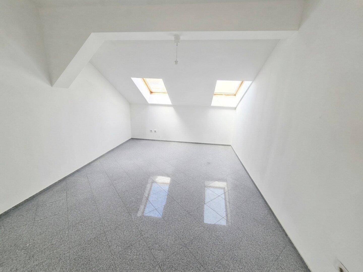 Heller, unmöblierter Raum mit zwei Dachfenstern und glänzendem Fliesenboden.
