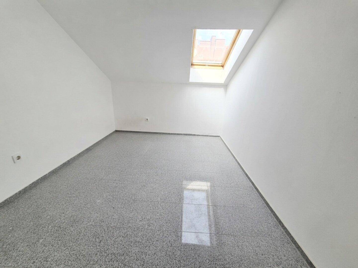 Leerer Raum mit einem Dachfenster und glänzendem, grauem Fliesenboden, ideal für Renovierung.