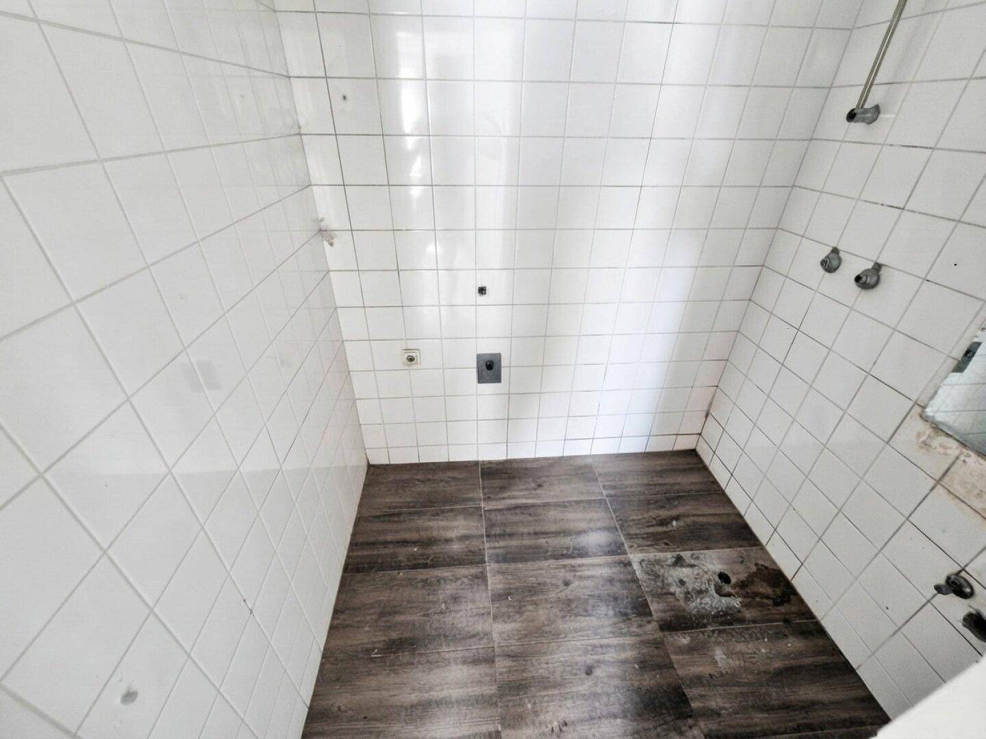 Unfertiger Duschbereich mit weißen Wandfliesen und dunklem Bodenbelag, bereit für die Installation.