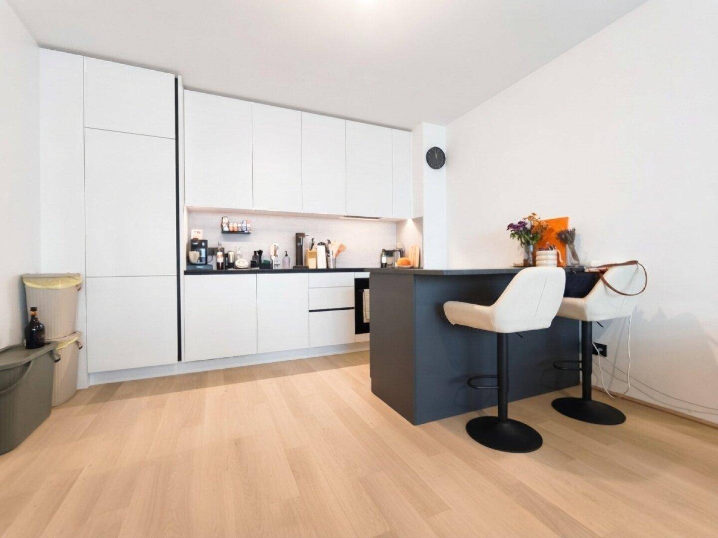 Moderne Küche mit weißen Hochglanzfronten, dunkler Kücheninsel und integrierter Frühstücksbar.