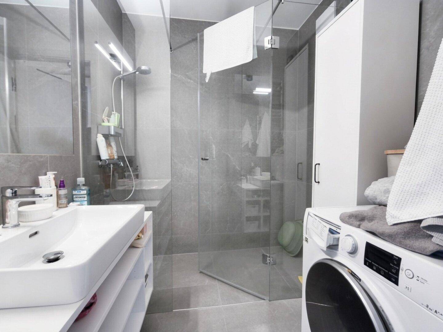 Modernes Badezimmer mit begehbarer Dusche, Waschbecken und integrierter Waschmaschine.