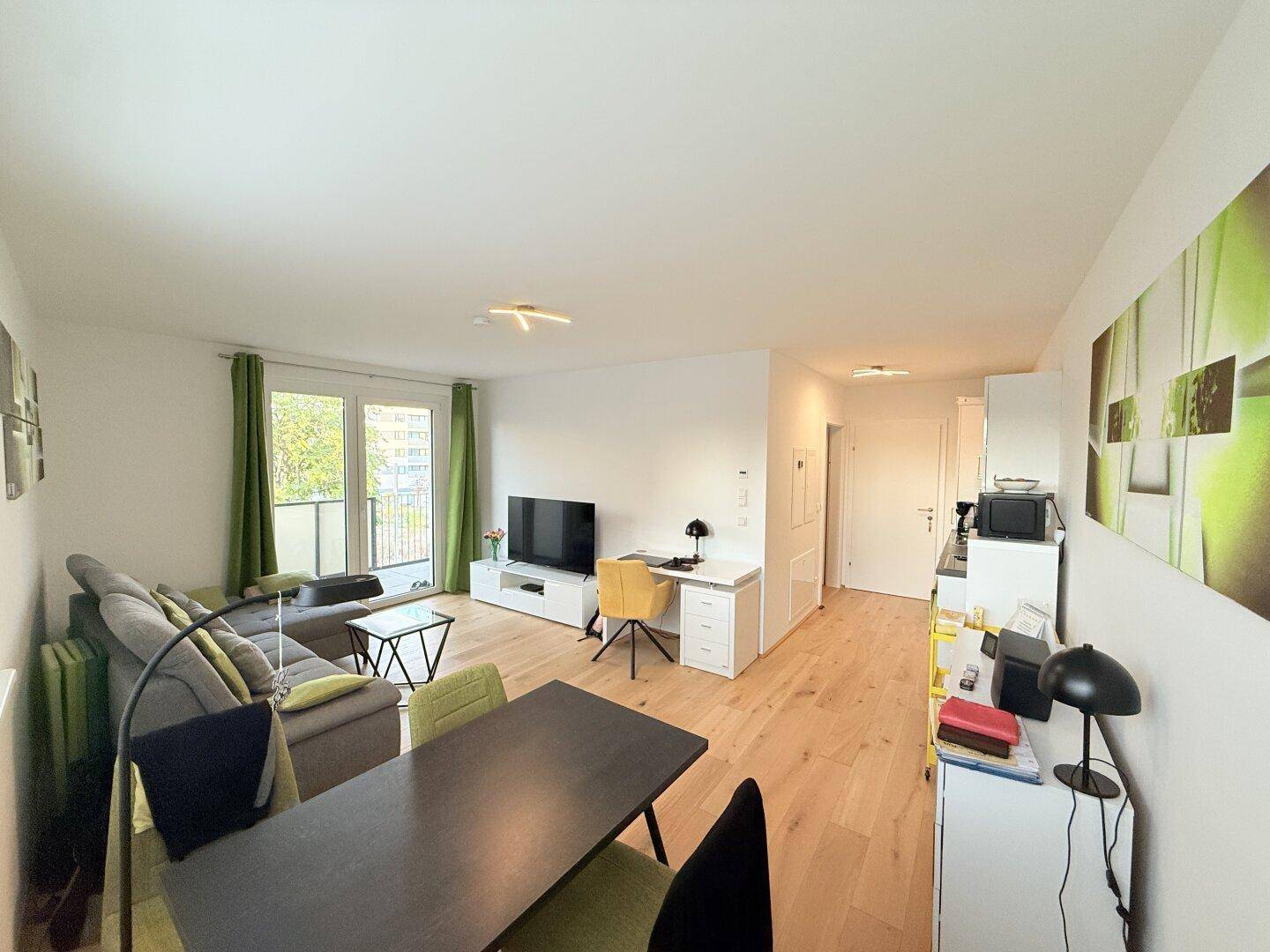 Heller Wohnbereich mit Sofa, Fernseher, Schreibtisch und Balkonzugang.