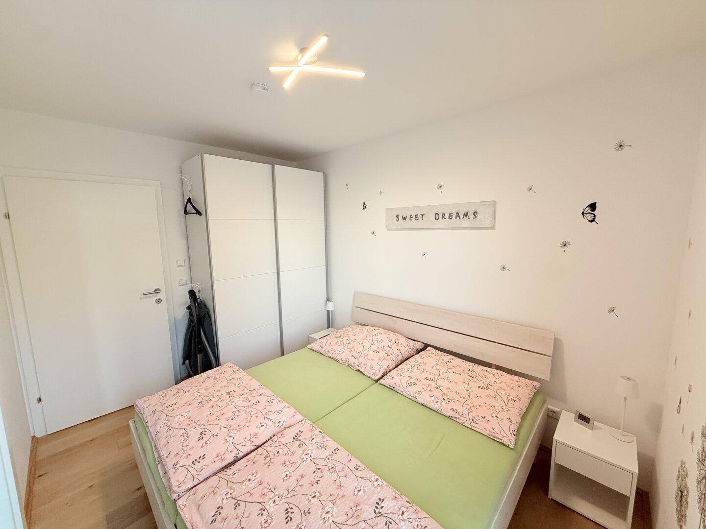 Schlafzimmer mit Doppelbett, weißem Kleiderschrank und Holzboden.