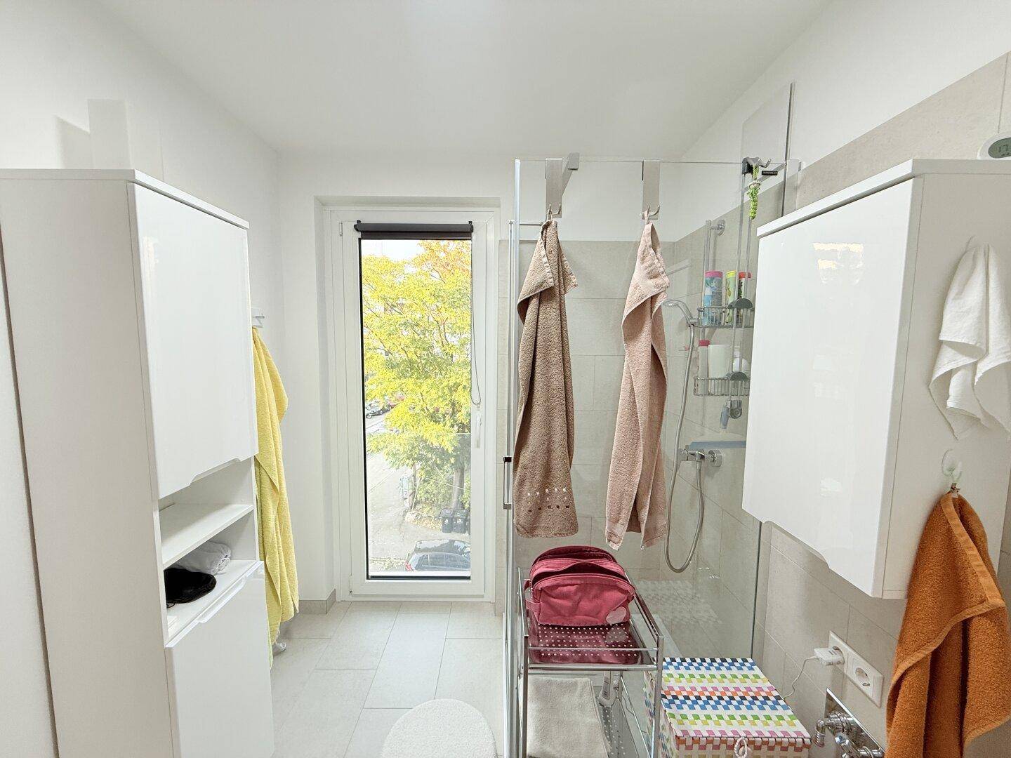 Helles Badezimmer mit Duschkabine, Fenster und Blick ins Grüne.