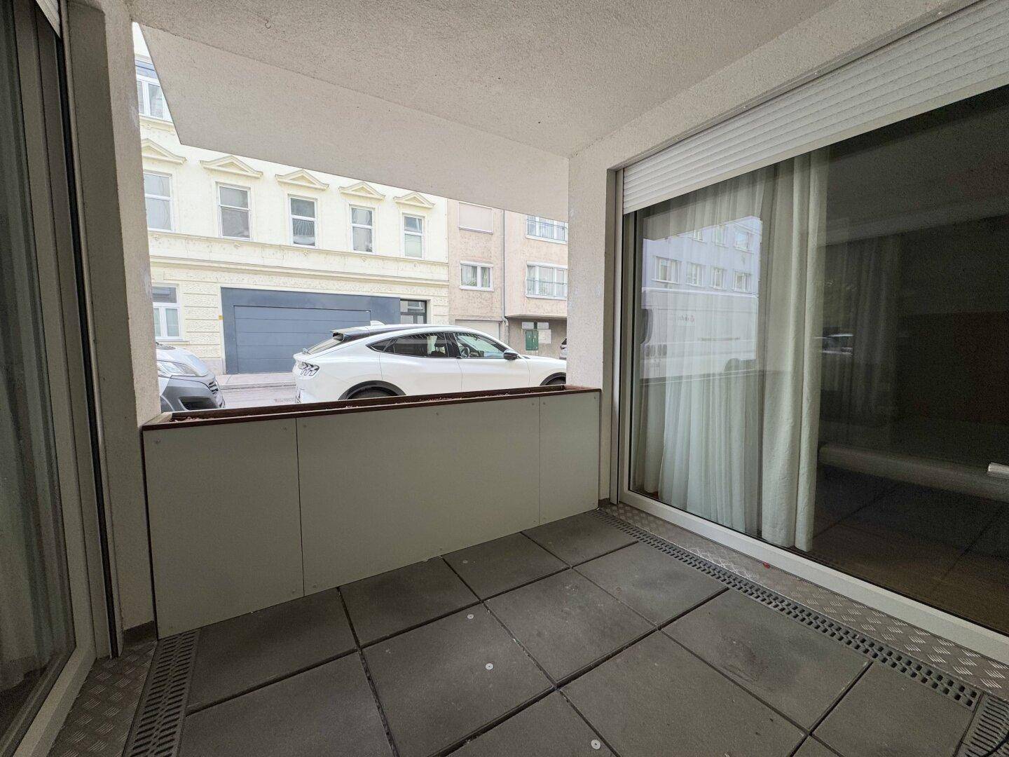 Kleiner Balkon mit Fliesenboden und Blick auf die Straße und die gegenüberliegenden Gebäude.