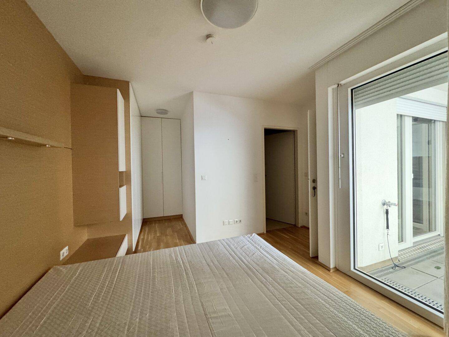 Helles Schlafzimmer mit Zugang zu einem Balkon und integrierten Schränken, ausgestattet mit Parkettboden.