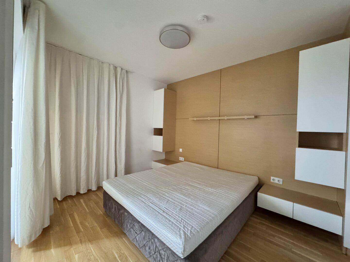 Schlafzimmer mit Holzboden, integrierten Holzpaneelen und modernen Einbauschränken, hell und funktional.