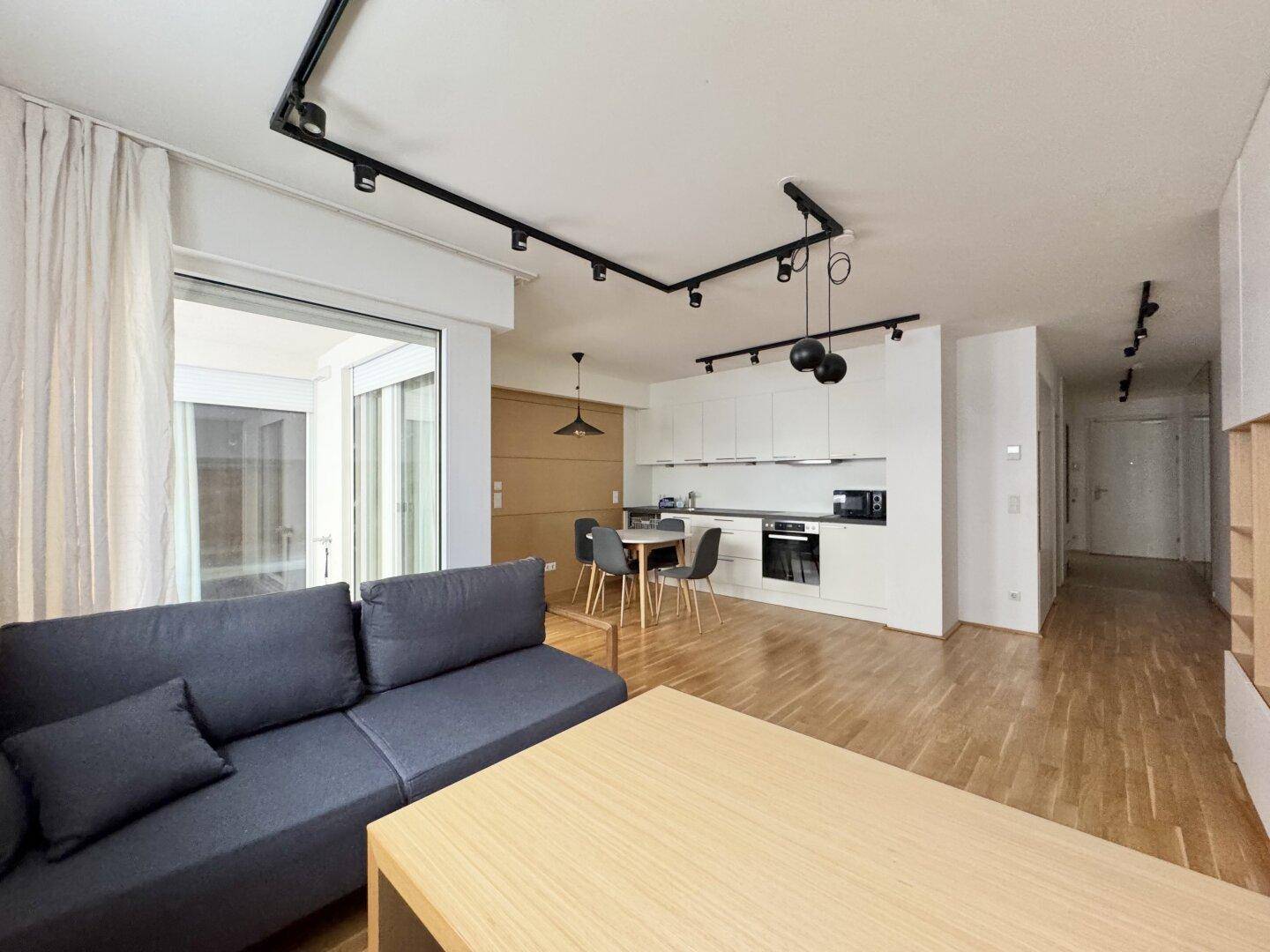 Moderner offener Wohn-Essbereich mit integrierter Küche, Parkettboden und Zugang zu einem Balkon.