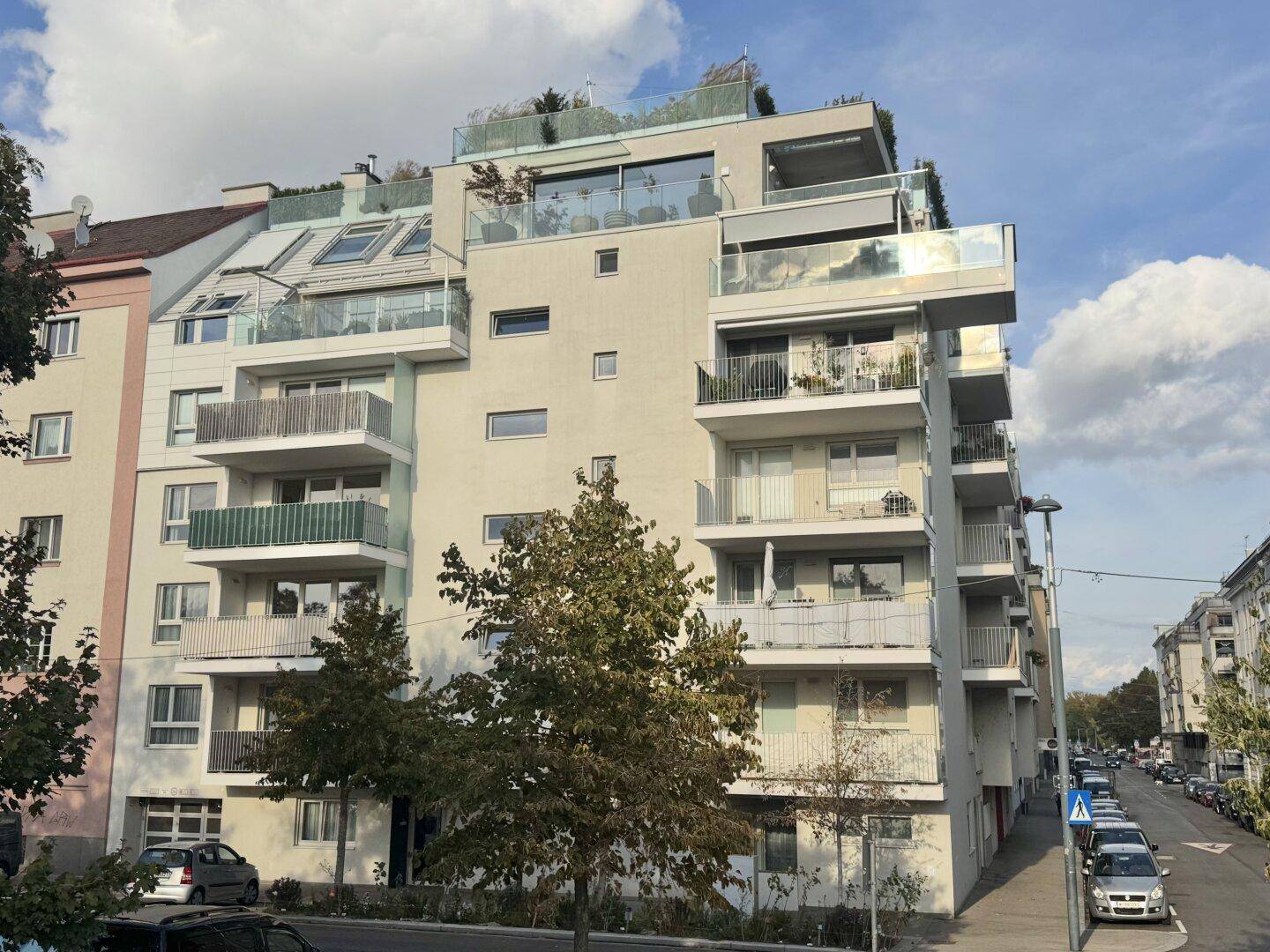 Modernes Mehrfamilienhaus mit mehreren Balkonen und Dachterrassen in einer städtischen Umgebung.