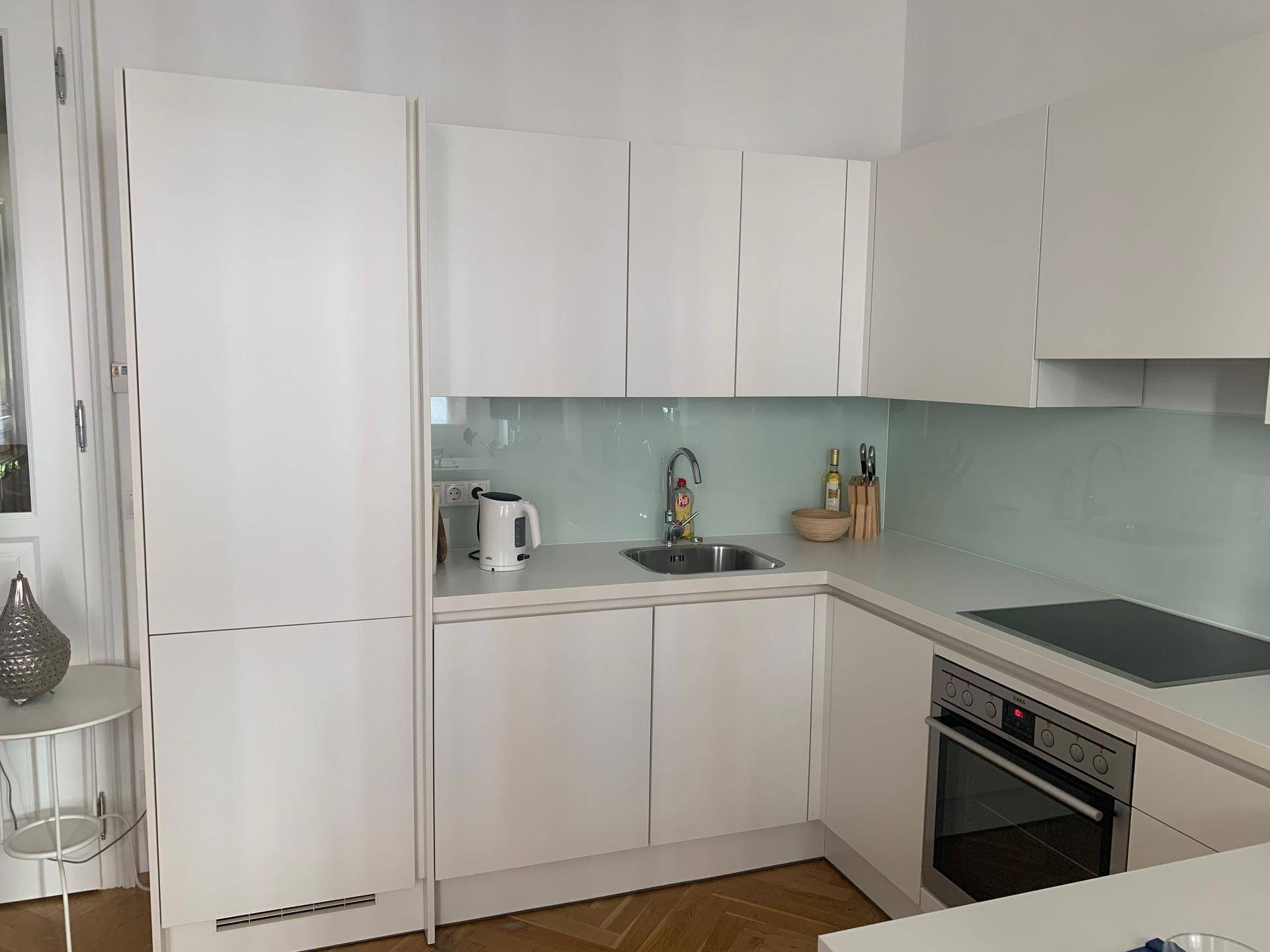 Funktionale weiße Küche mit Spülbecken, Kochfeld und integriertem Kühlschrank, ausgestattet für den täglichen Gebrauch.