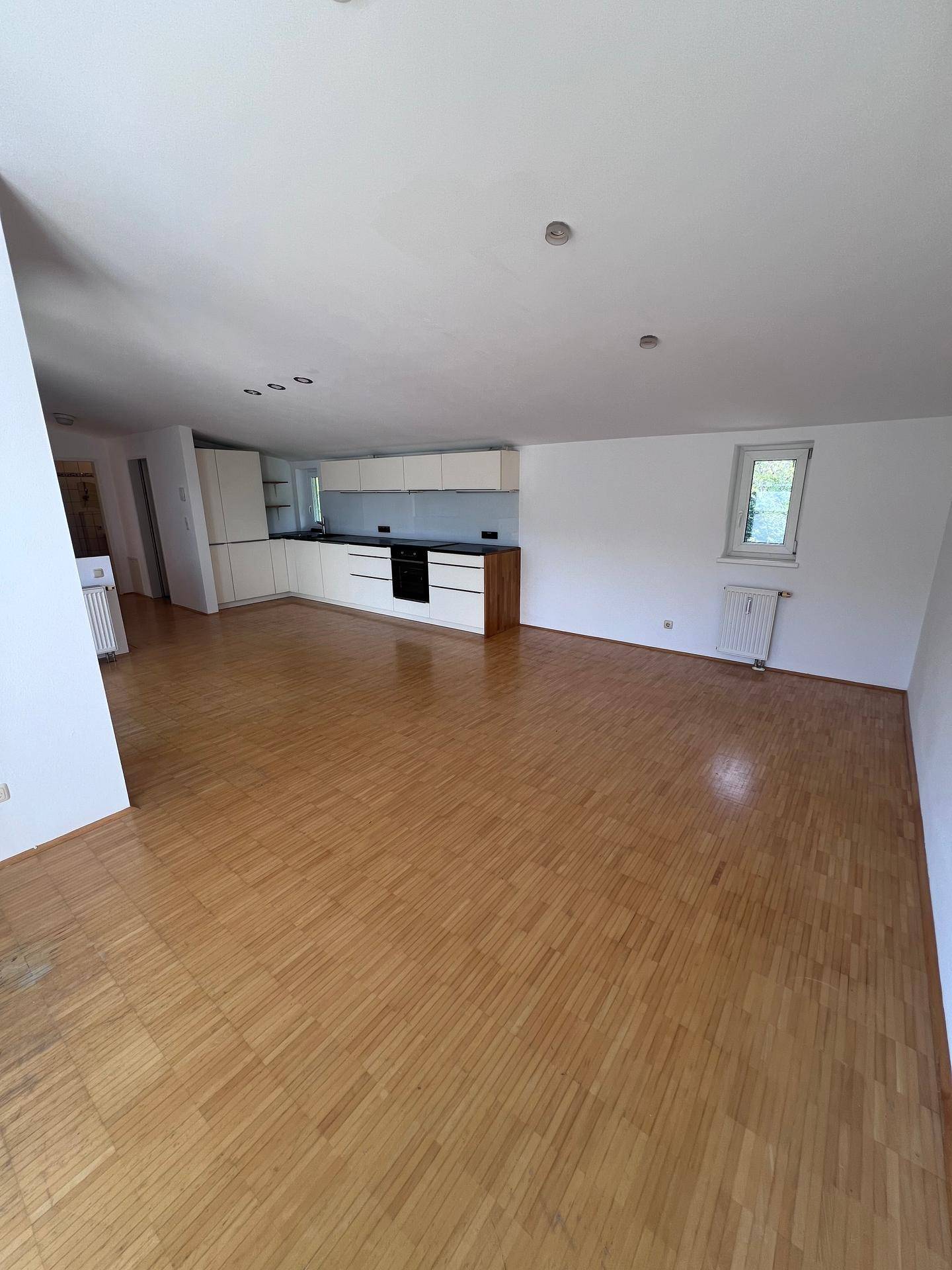 Geräumiger offener Wohnbereich mit integrierter Küche, Holzboden und einem Fenster für Tageslicht.
