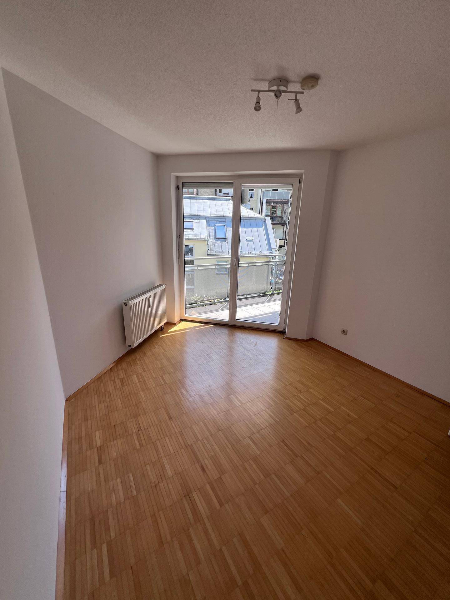 Geräumiges Zimmer mit Holzboden und großem Balkonzugang, der viel natürliches Licht spendet.