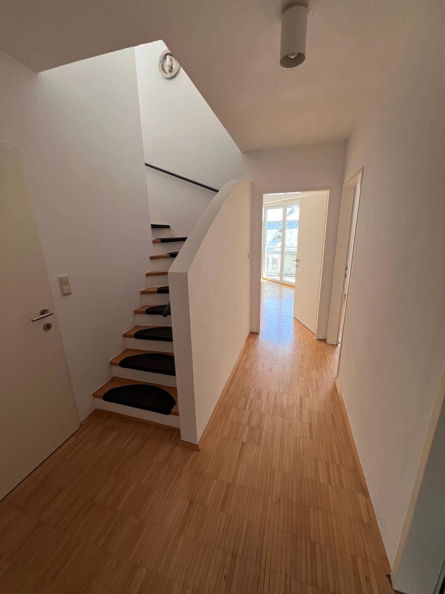 Heller Flur mit Holzparkettboden und einer Treppe, die in die obere Etage führt.