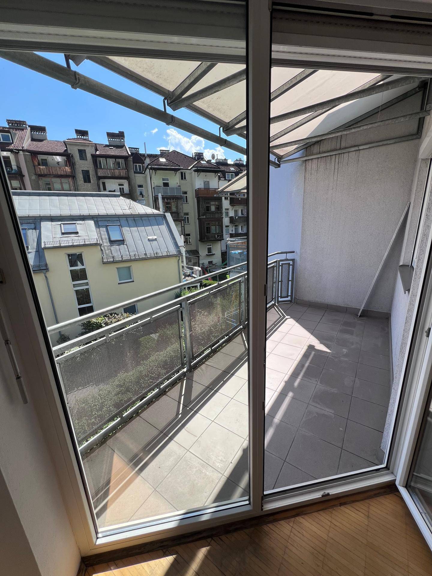Heller Balkon mit Fliesenboden und Metallgeländer, bietet einen Blick auf die umliegenden Gebäude.