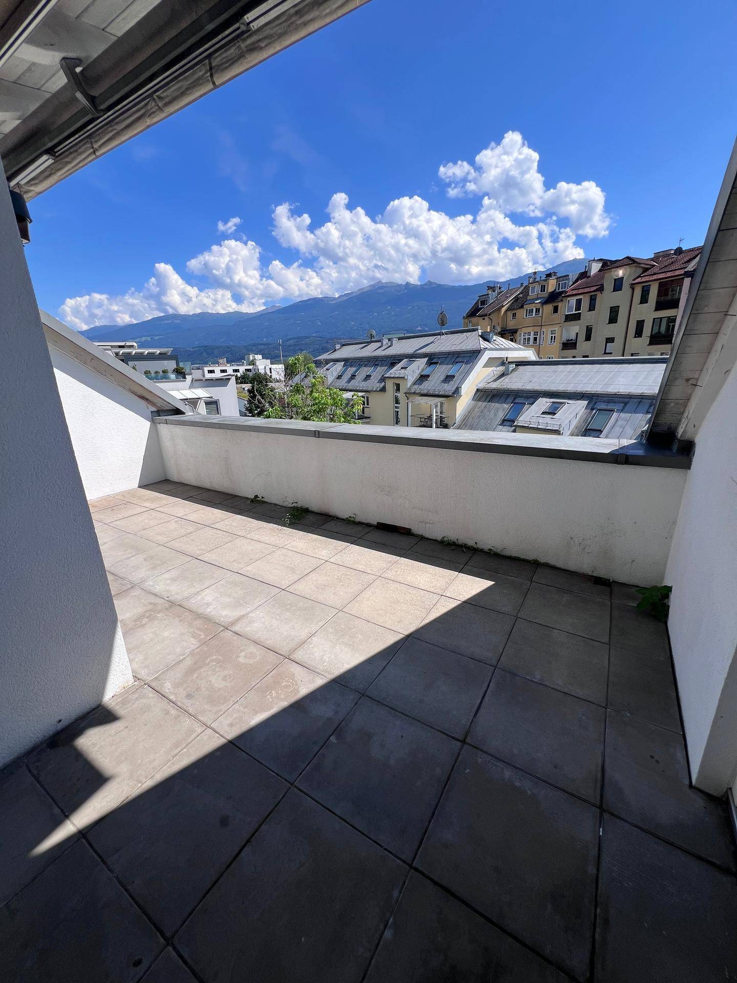 Große Dachterrasse mit Fliesenboden und Panoramablick auf die Berge und die Stadt.