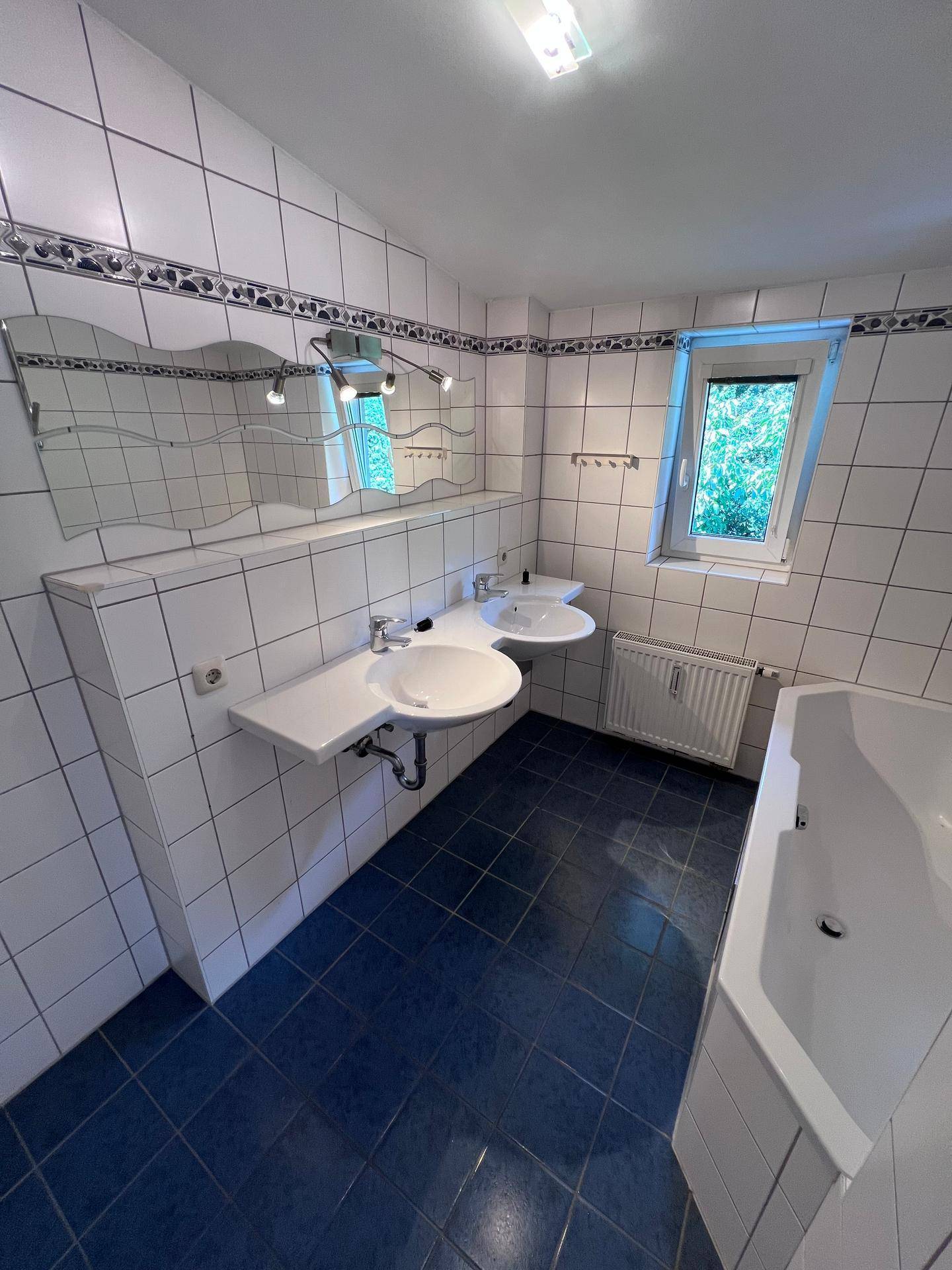 Geräumiges Badezimmer mit Eckbadewanne, Doppelwaschbecken, großem Spiegel und Fenster.