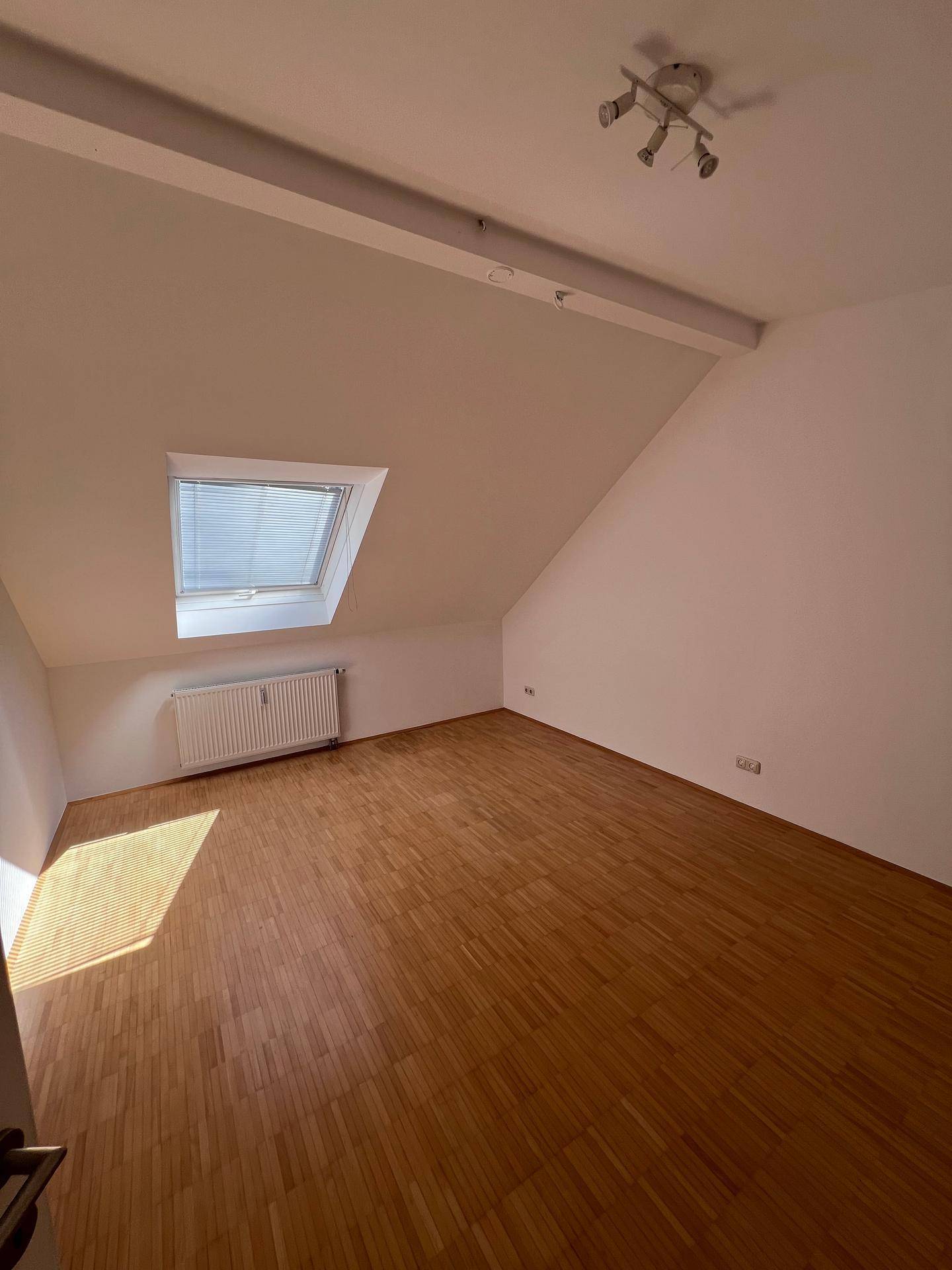 Gemütliches Schlafzimmer im Dachgeschoss mit schräger Decke, Dachfenster und Holzboden.