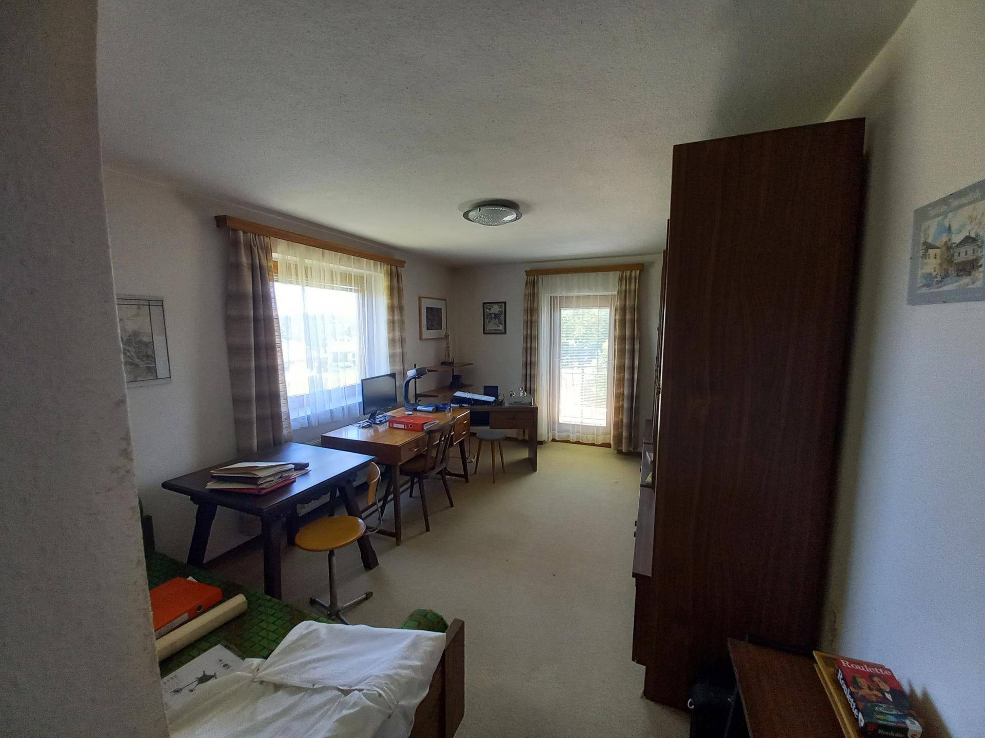Helles Arbeitszimmer mit zwei Schreibtischen, Teppichboden und Zugang zu einem Balkon oder Garten.