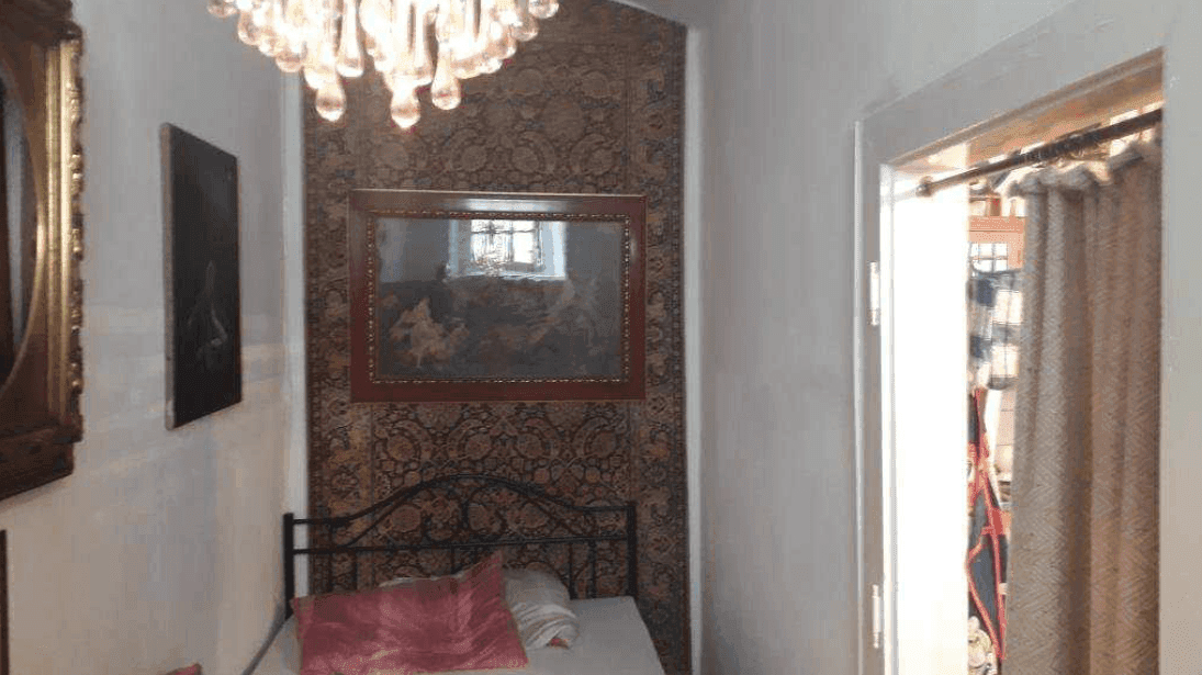 Schlafzimmer mit einem Einzelbett, gemusterter Tapete und einem Kronleuchter, passend zum traditionellen Stil.