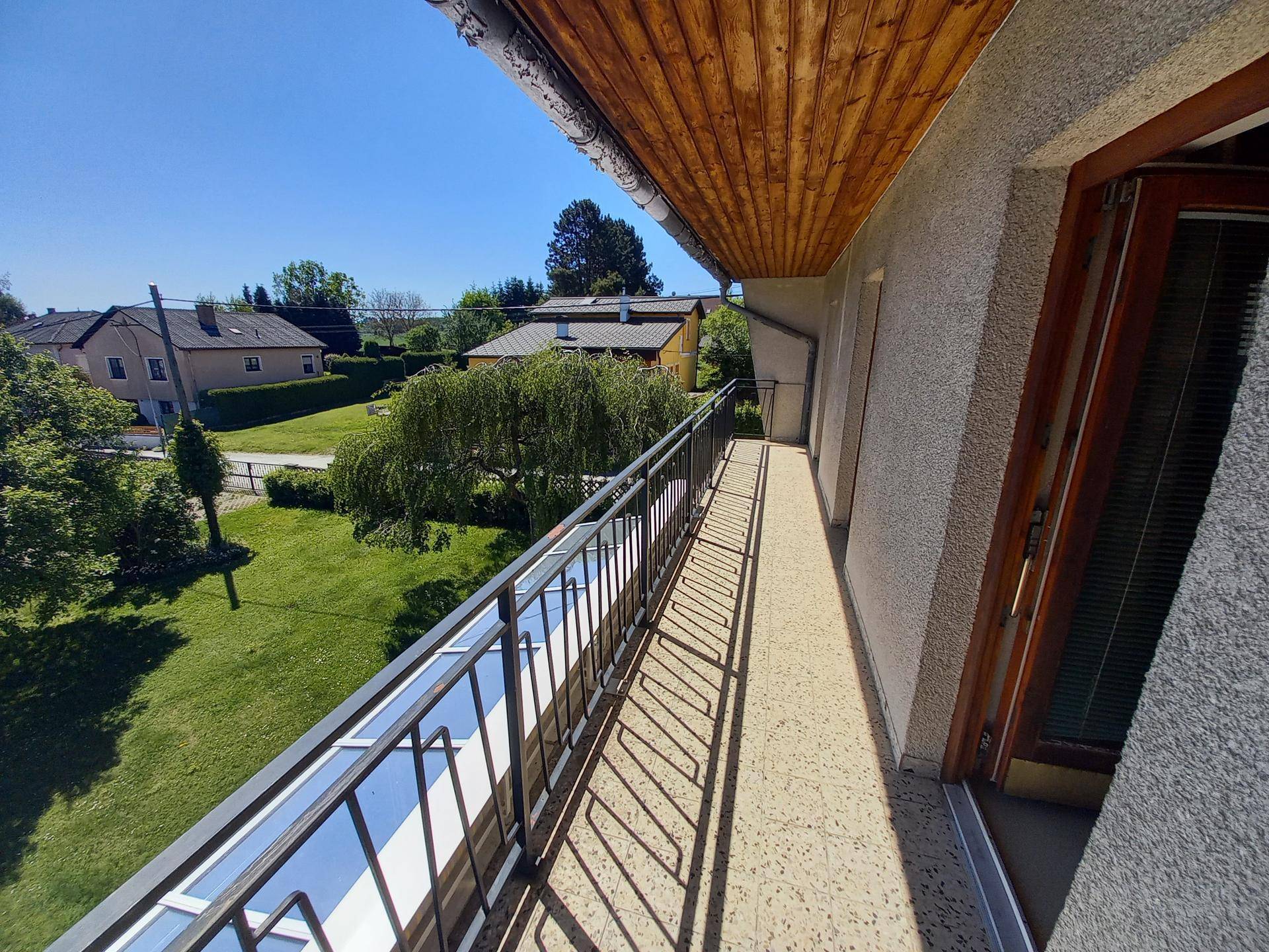Langer Balkon mit Metallgeländer und Holzdach, der einen weiten Blick ins Grüne ermöglicht.