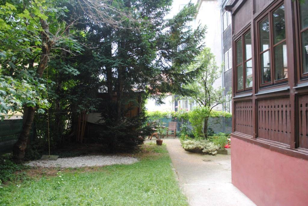 Weiterer Blick in den grünen Garten mit Bäumen, einer Schaukel und einem Teil des Gebäudes.