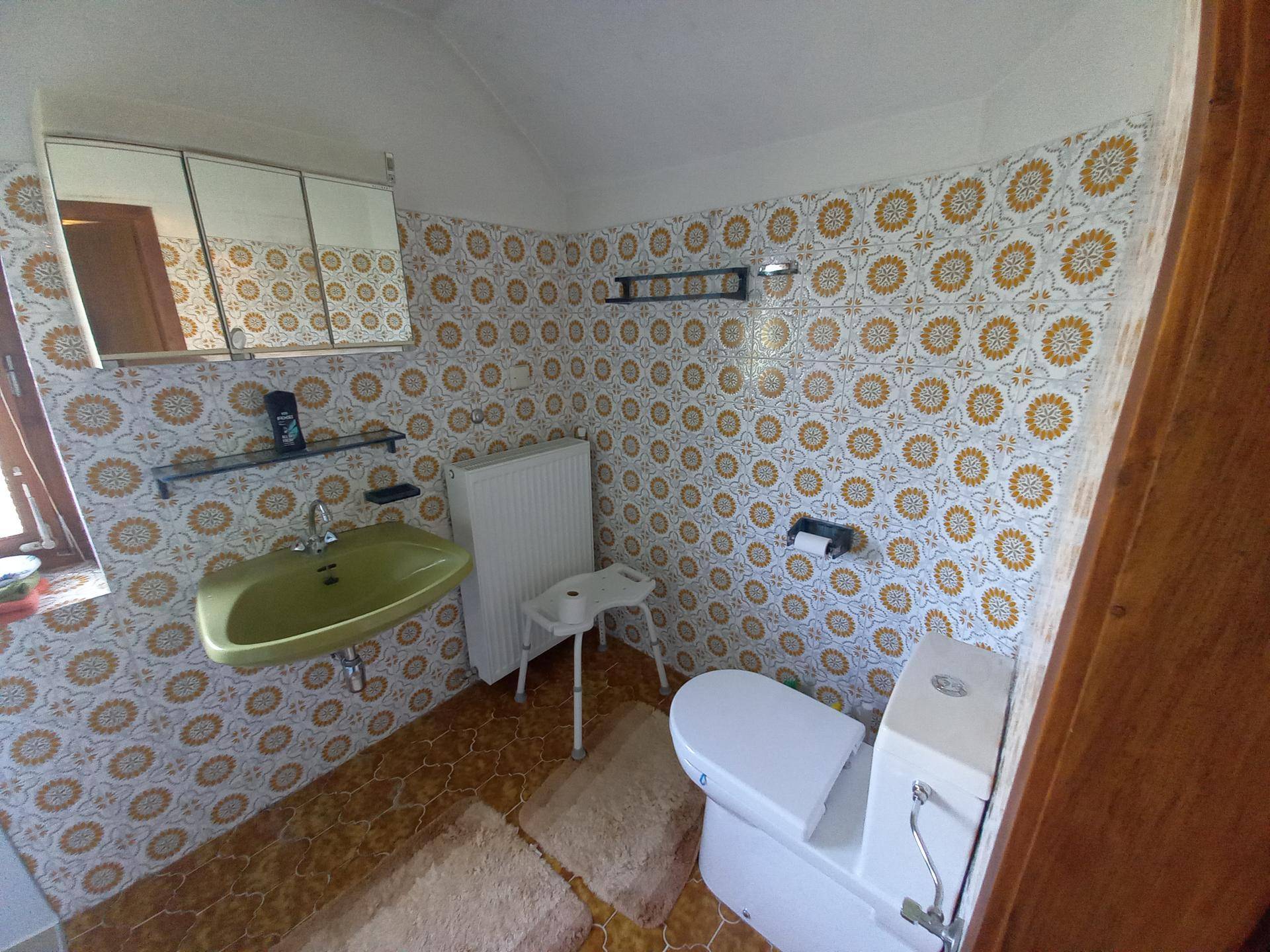 Kleines WC mit auffälligen gemusterten Fliesen, grünem Waschbecken und Fenster.