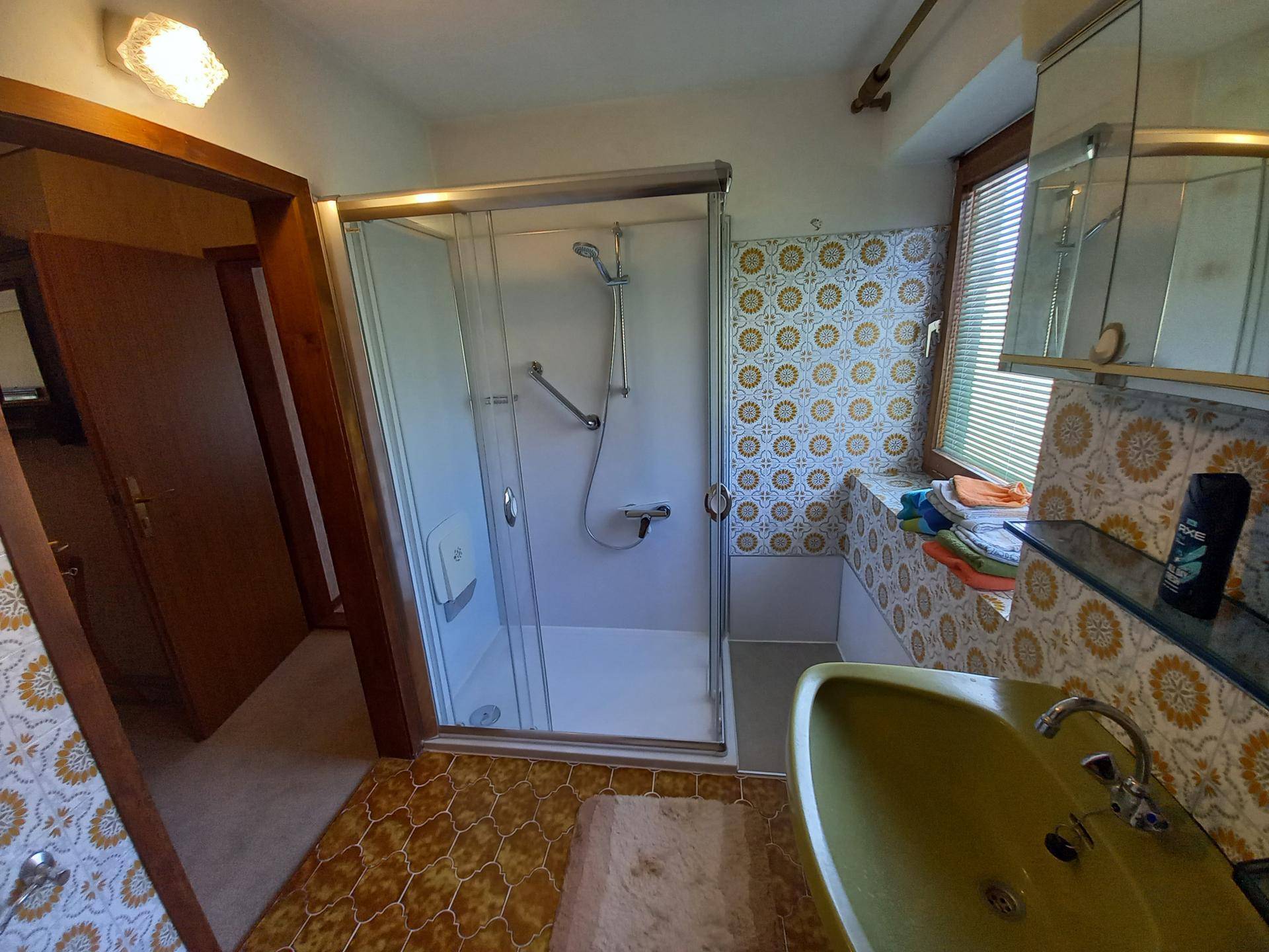 Badezimmer mit Duschkabine, grünem Waschbecken und gemusterten Fliesen im Retro-Stil.