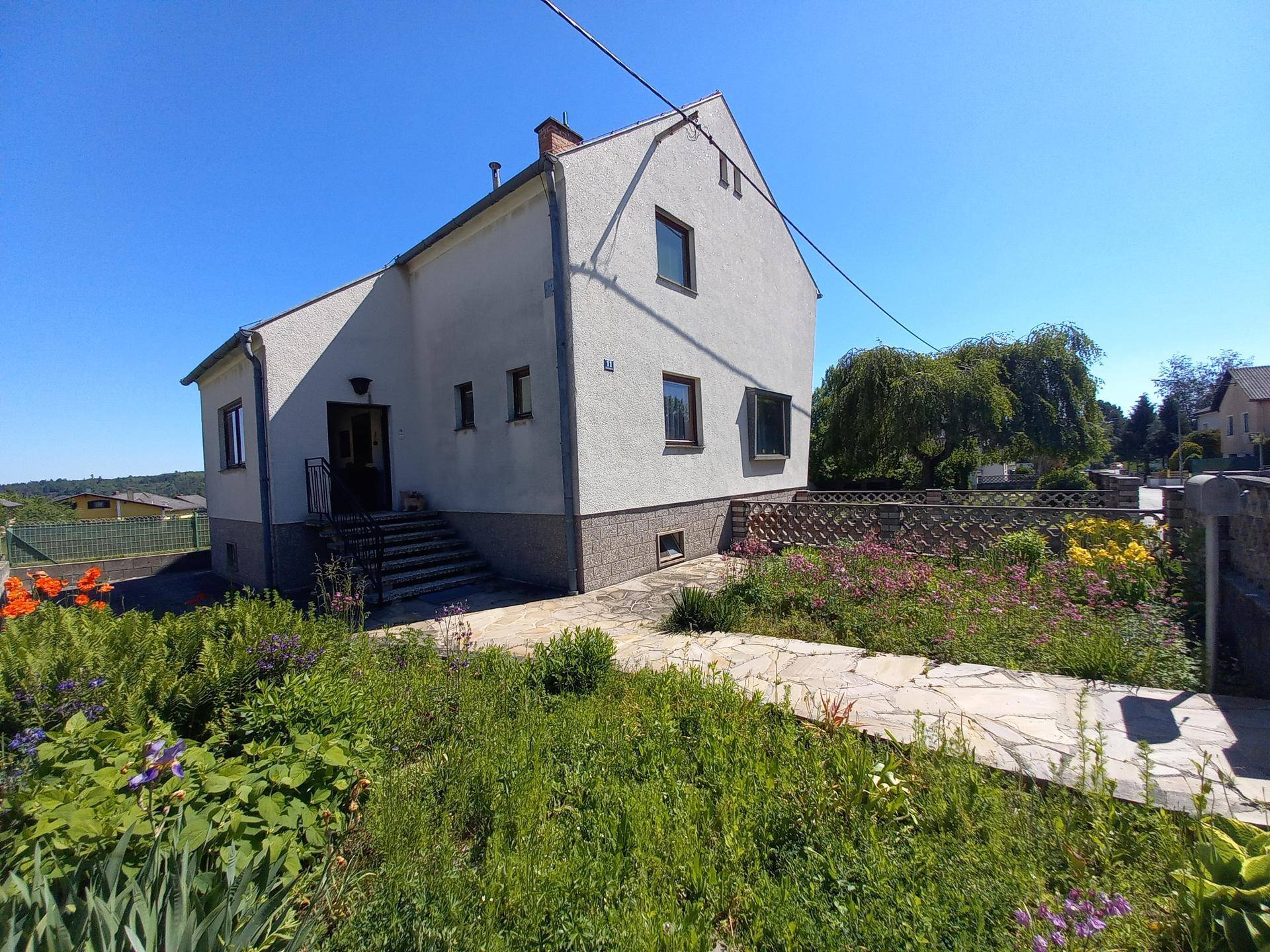Seitenansicht des Hauses mit gepflegtem Vorgarten und Zugang über eine Steintreppe.