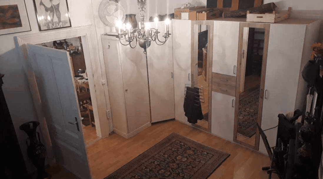Schlafzimmer mit großen Spiegelschränken, Holzboden und einem Kronleuchter an der Decke, typisch für einen Altbau.