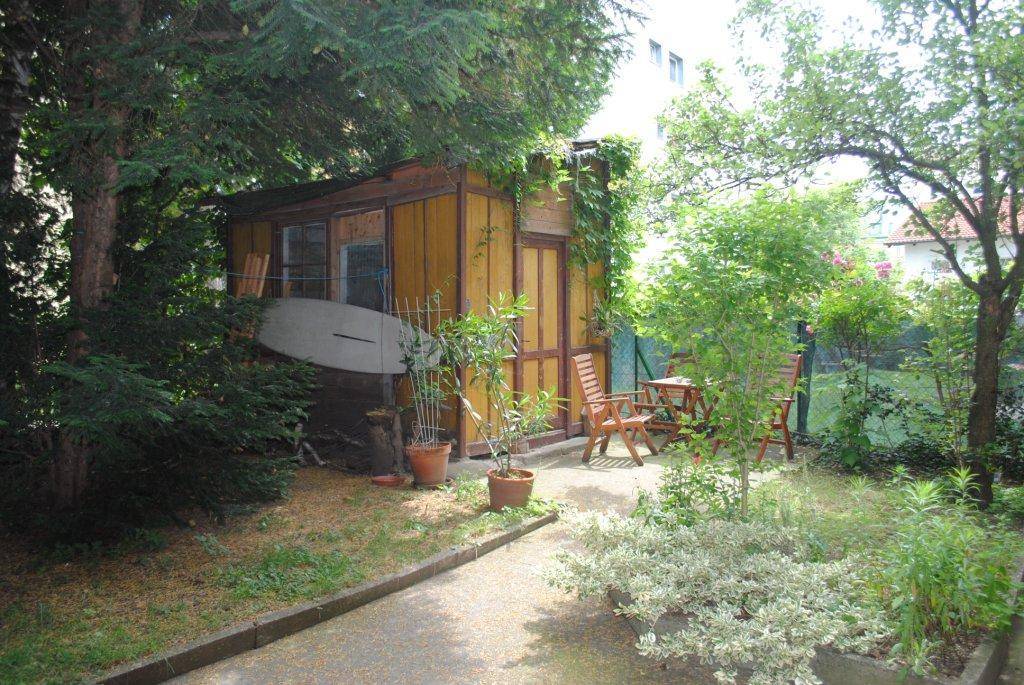 Gemütlicher Gartenbereich mit Holzschuppen, Sitzgelegenheiten und üppiger Vegetation.