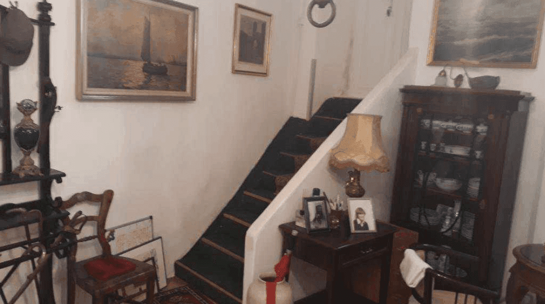 Traditioneller Flur mit Holztreppe, antiken Möbeln und gerahmten Kunstwerken an den Wänden des Altbaus.