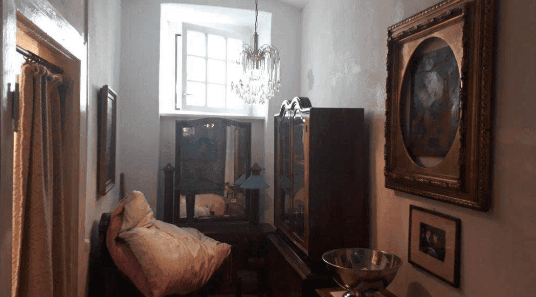 Gemütliches Schlafzimmer mit einem Fenster, das Tageslicht hereinlässt, und traditionellen Möbeln in einem Altbau.