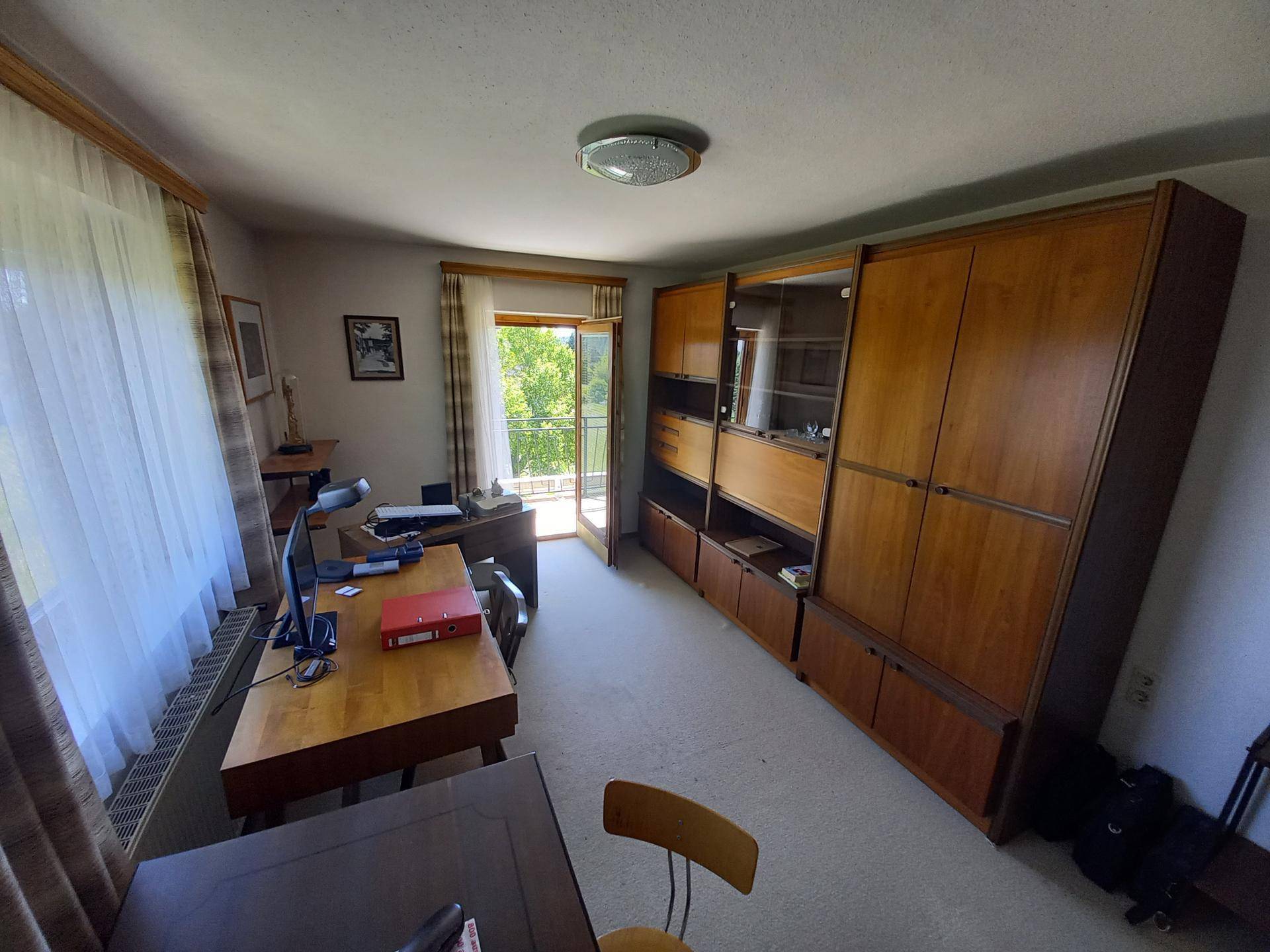Arbeitszimmer mit großem Holzschrank und Zugang zum Balkon.