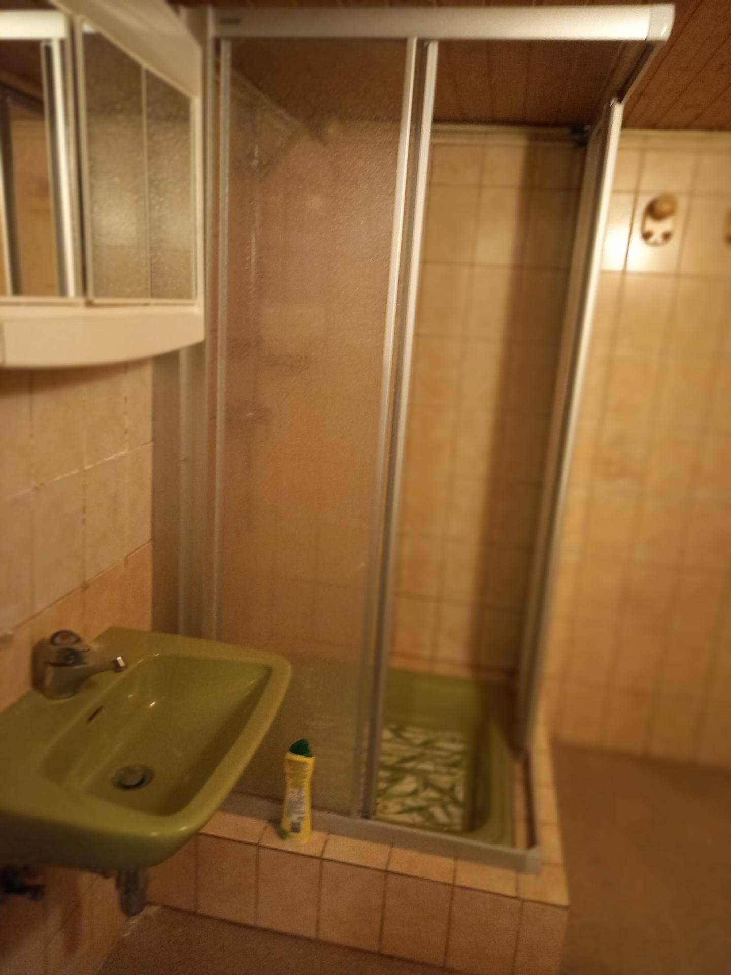 Kleines Badezimmer mit Duschkabine und Waschbecken, älterer Ausstattung.