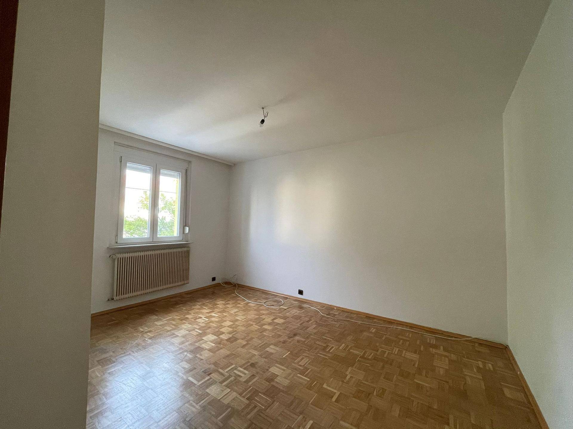 Leeres Schlafzimmer mit klassischem Fischgrätparkett und einem Fenster für Tageslicht.