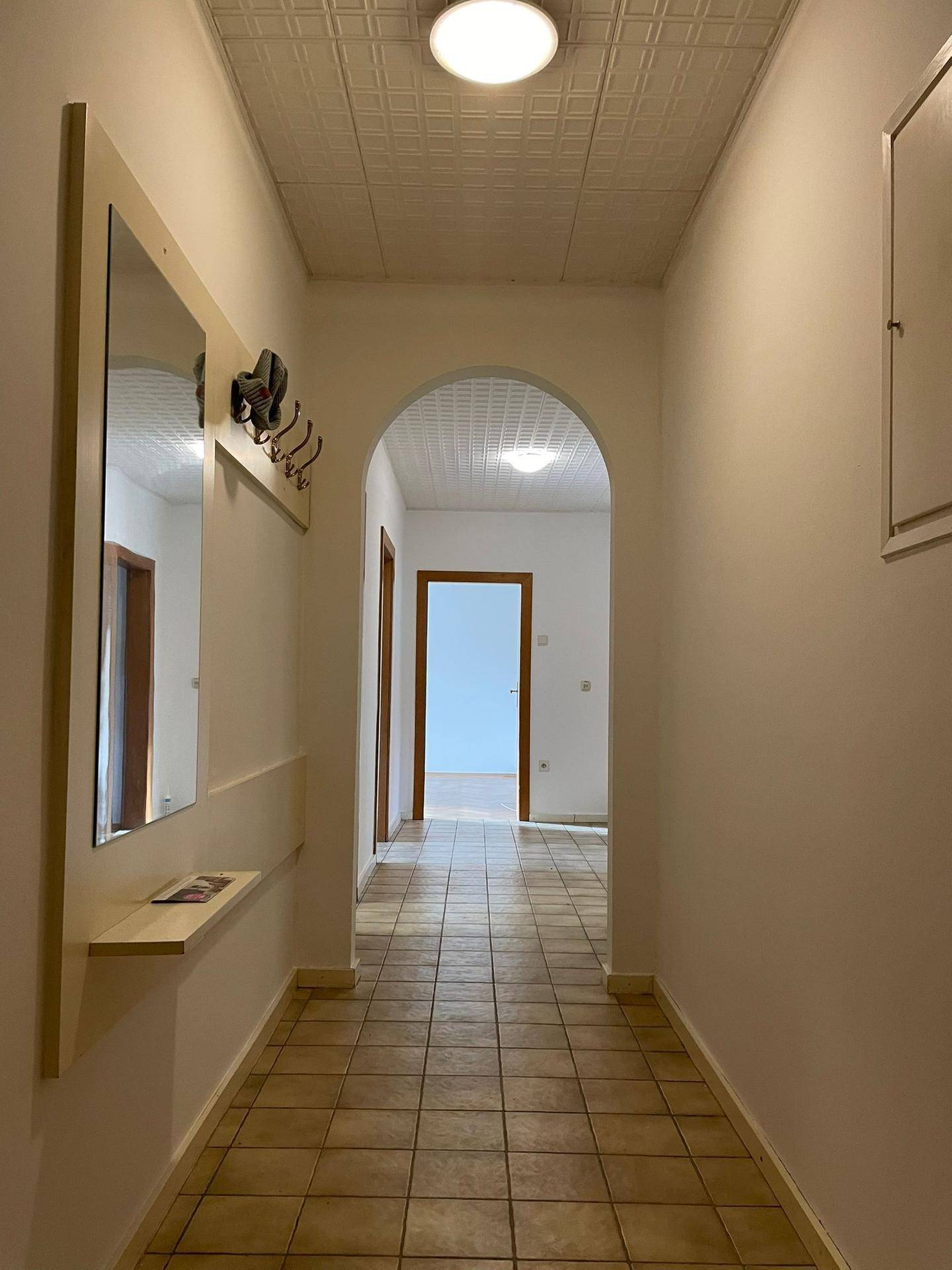 Heller Flur mit Fliesenboden, Bogendurchgang und praktischer Garderobe mit Spiegel.