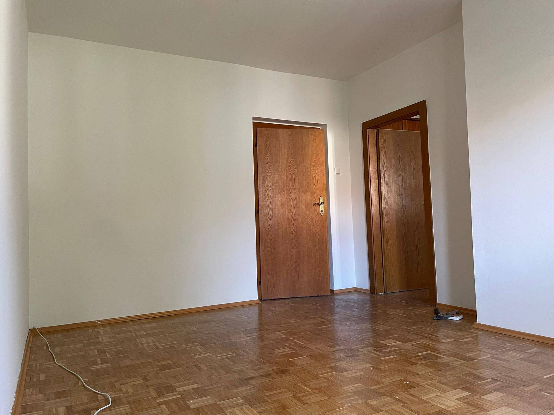 Heller Raum mit Fischgrätparkettboden und zwei Holztüren, bereit zur individuellen Gestaltung.
