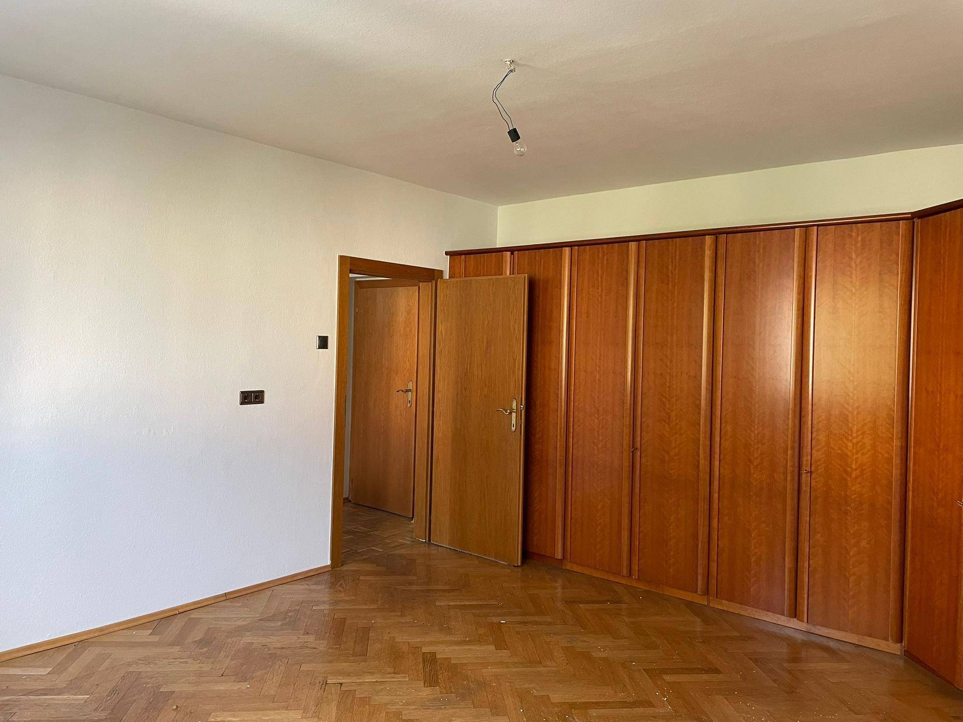 Schlafzimmer mit Fischgrätparkett, Holztür und praktischen Einbauschränken.