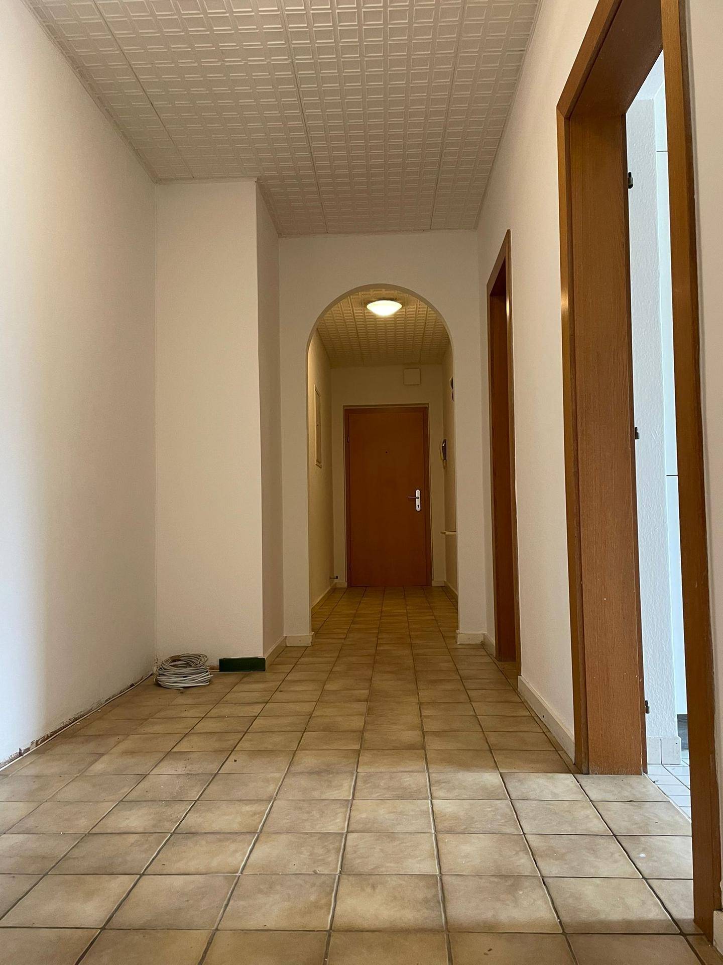 Langer Flur mit Fliesenboden und einem eleganten Bogendurchgang zu weiteren Räumen.