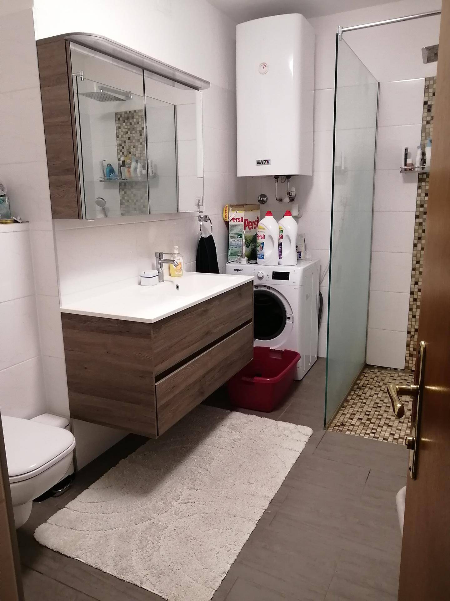 Modernes Badezimmer mit schwebendem Waschtisch, Spiegelschrank, Dusche und Waschmaschine.