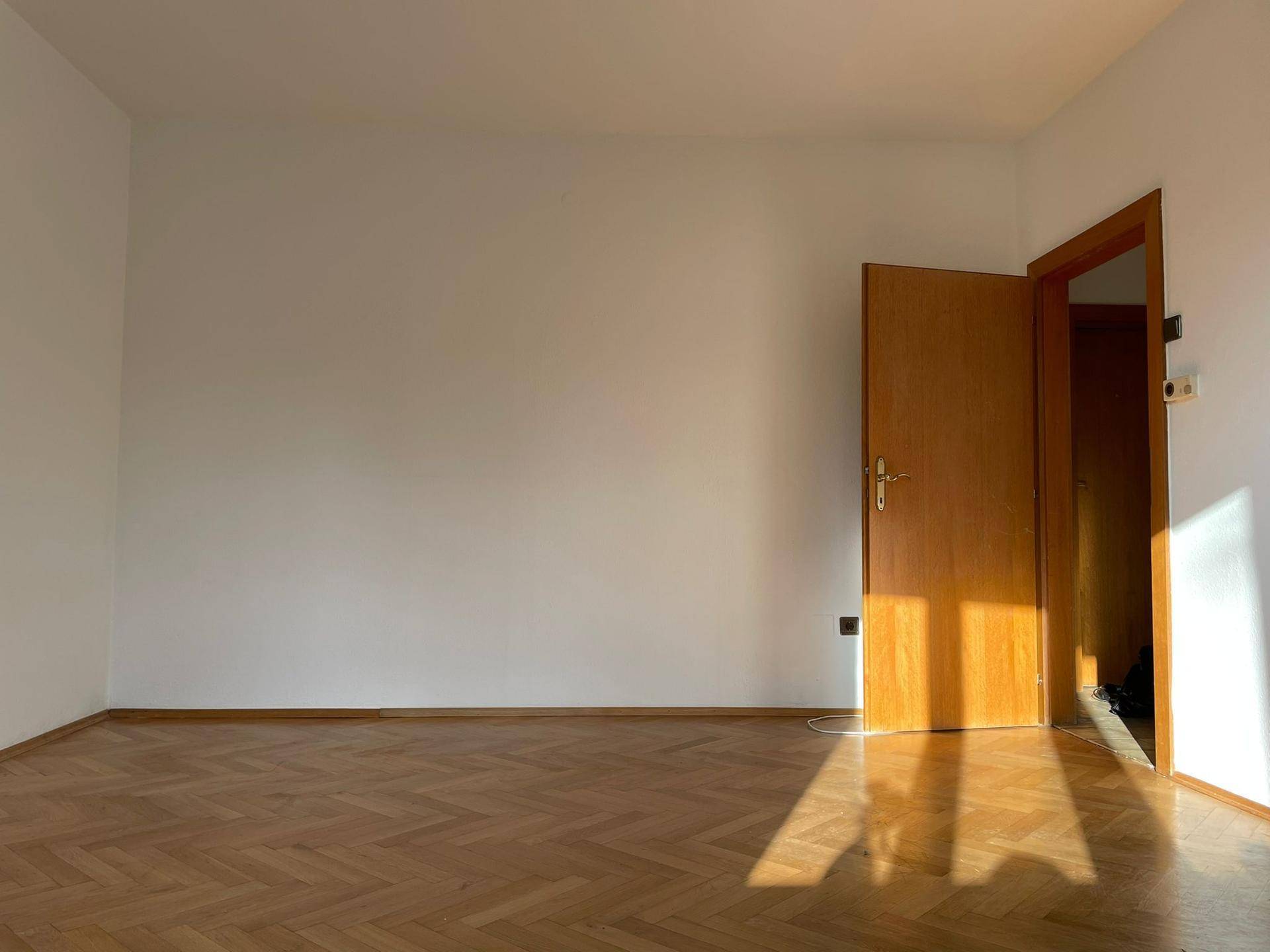 Helles, leeres Zimmer mit Fischgrätparkettboden und viel natürlichem Sonnenlicht.