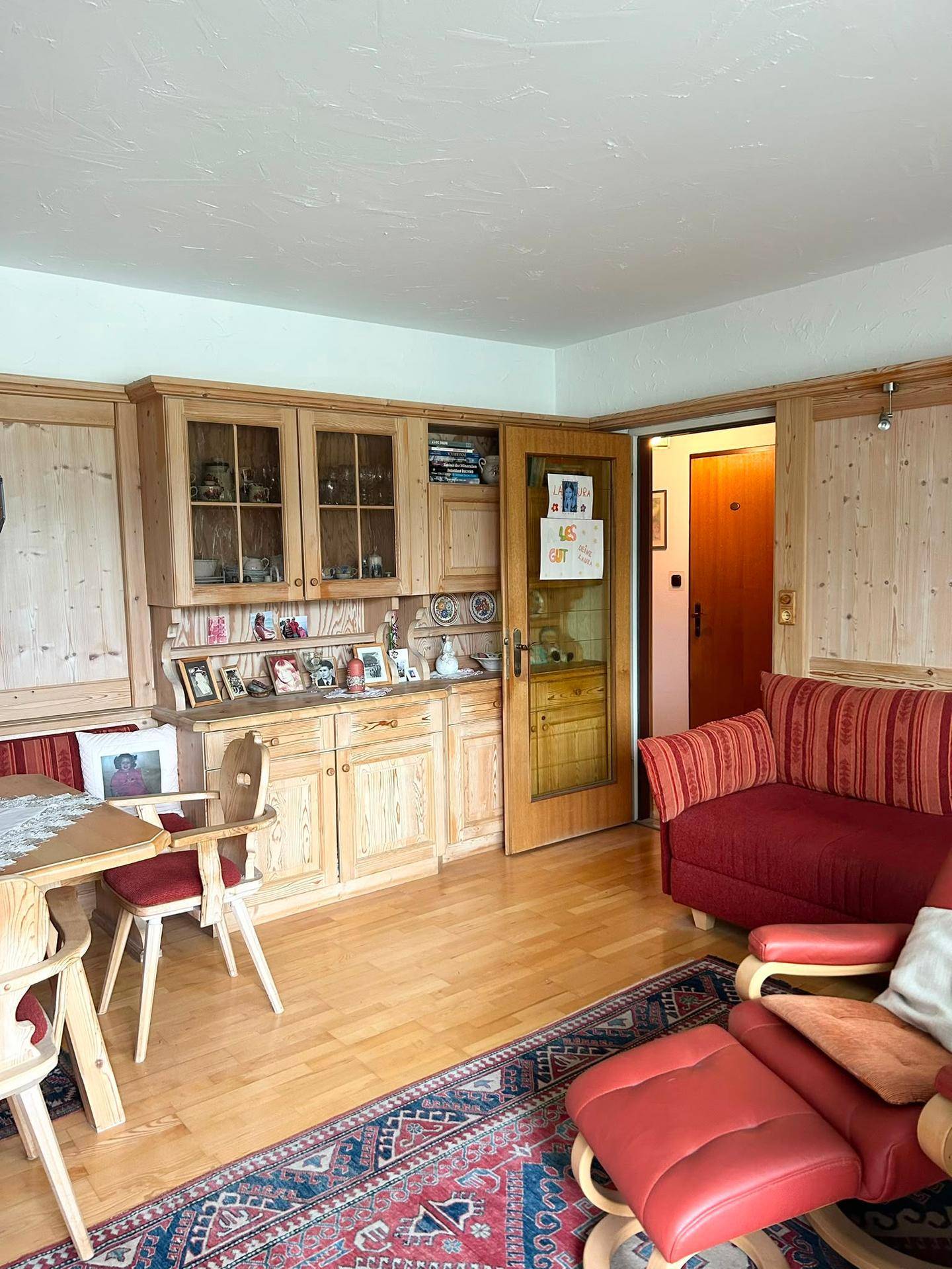 Gemütliches Wohnzimmer im alpinen Stil mit Holzmöbeln, rotem Sofa und traditionellem Teppich.